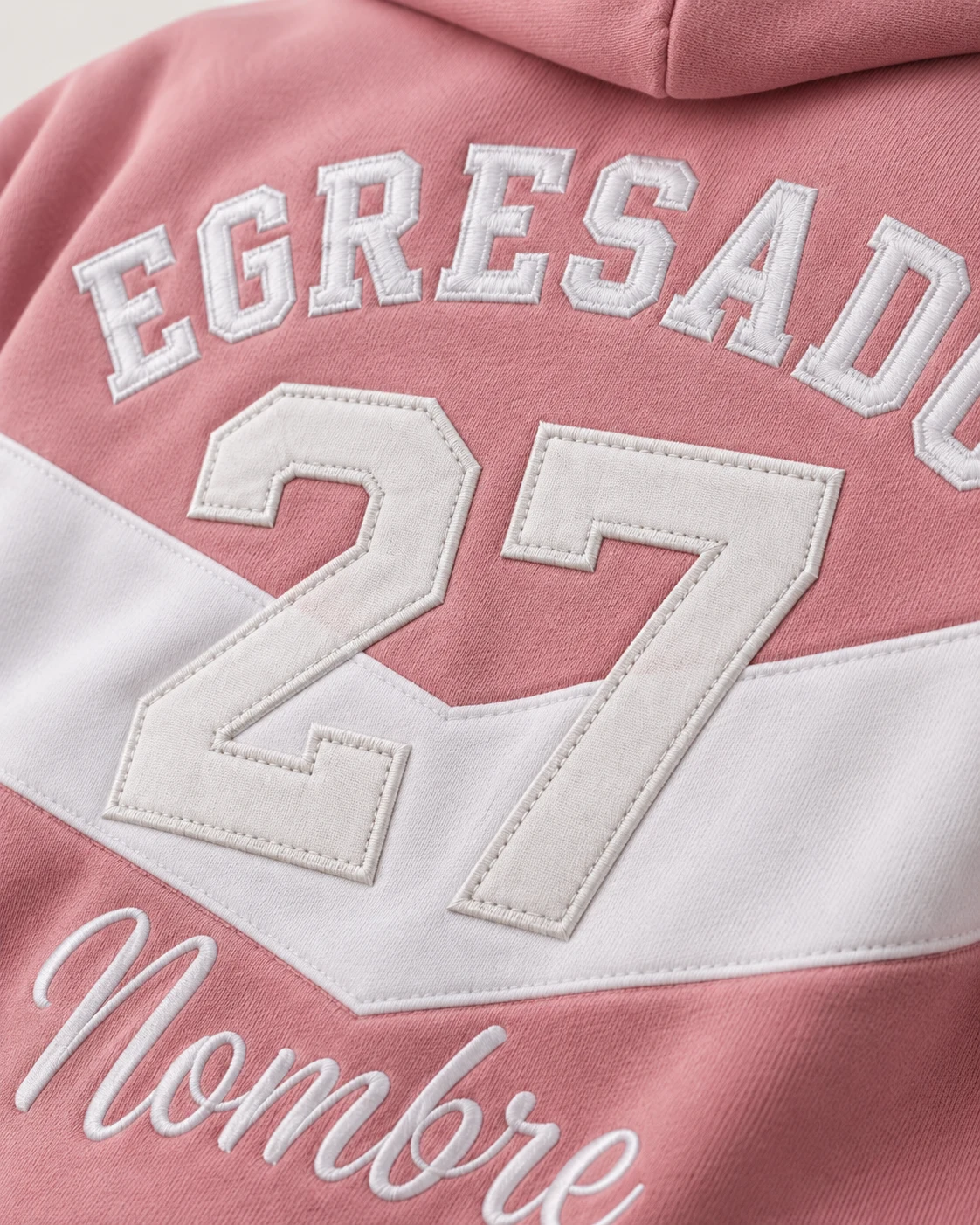 Campera rosa con franja blanca de frisa premium, letras bordadas y parche del año 27 cosido. Vista de detalle.