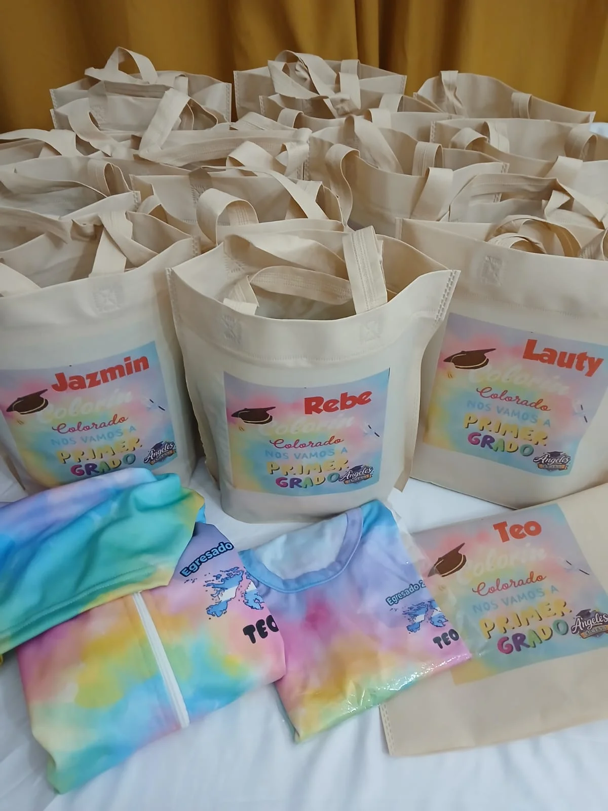 Campera, remera y bolsas personalizadas de un pedido, en tonos pastel.