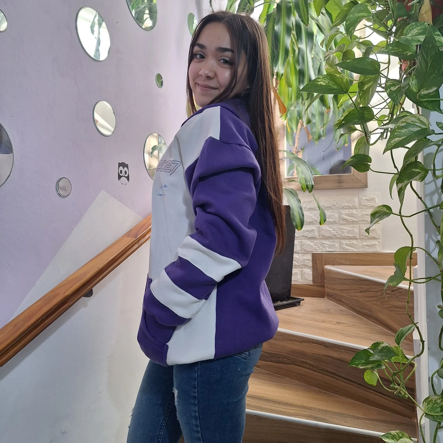 Joven mostrando un buzo violeta y blanco junto a una escalera.