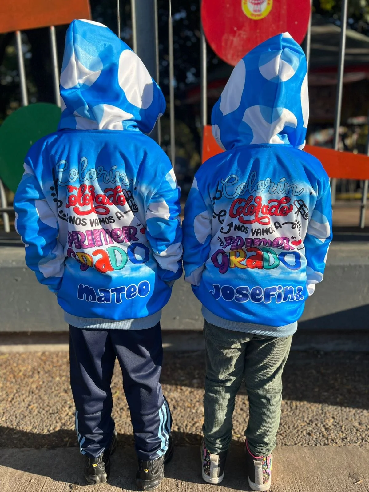 Dos chicos de espaldas con camperas celestes personalizadas para su egreso de jardín.