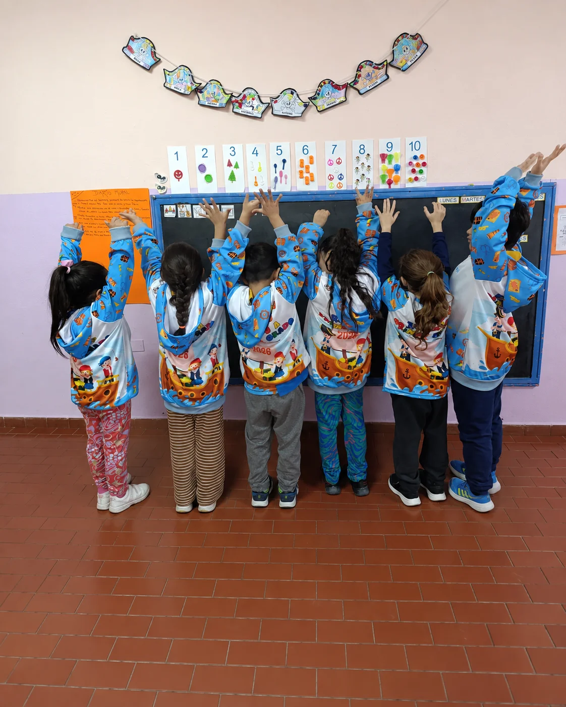 Un grupo en el aula levantando los brazos con sus camperas de egresados con dibujos de piratas.