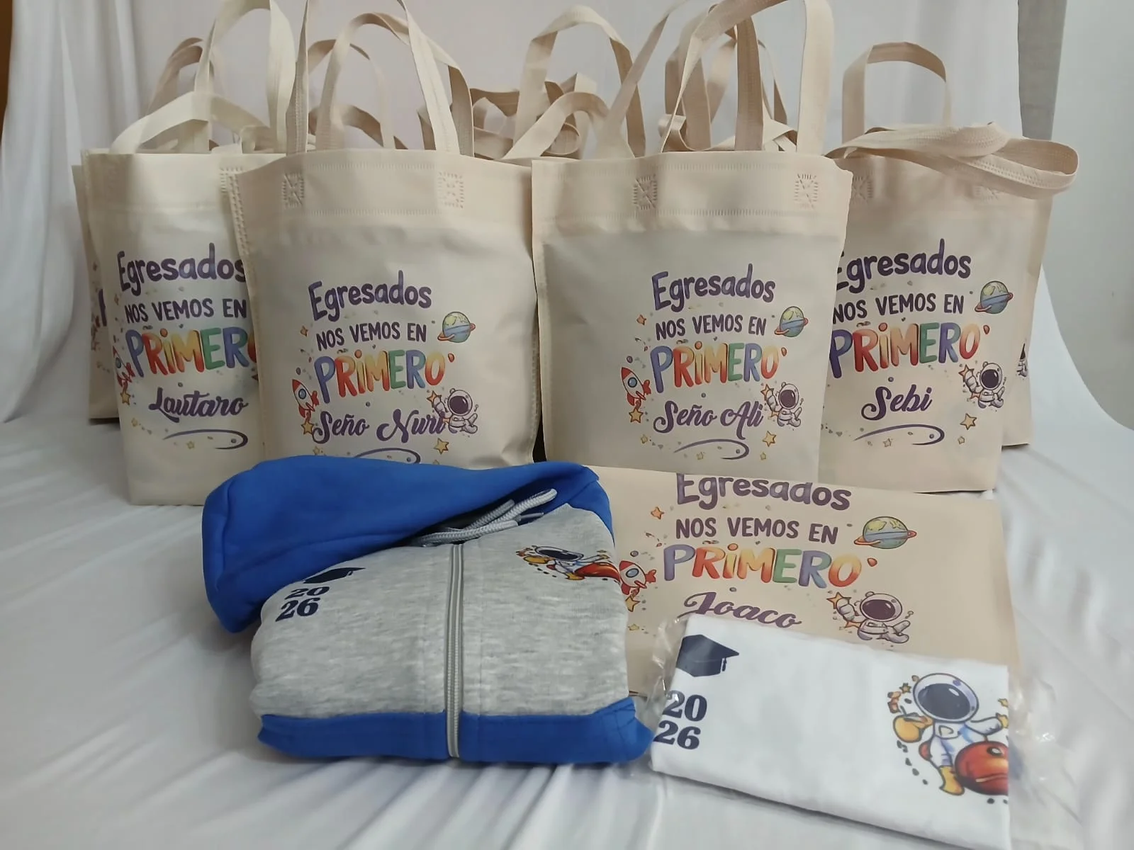Campera gris y azul, remera y bolsas con diseños de astronautas para egresados.