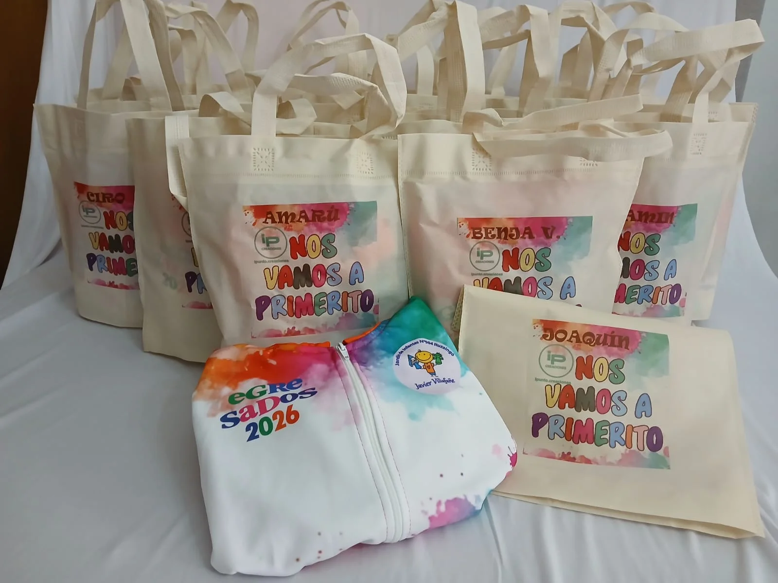 Campera blanca con detalles multicolor y bolsas de egresados 2026.